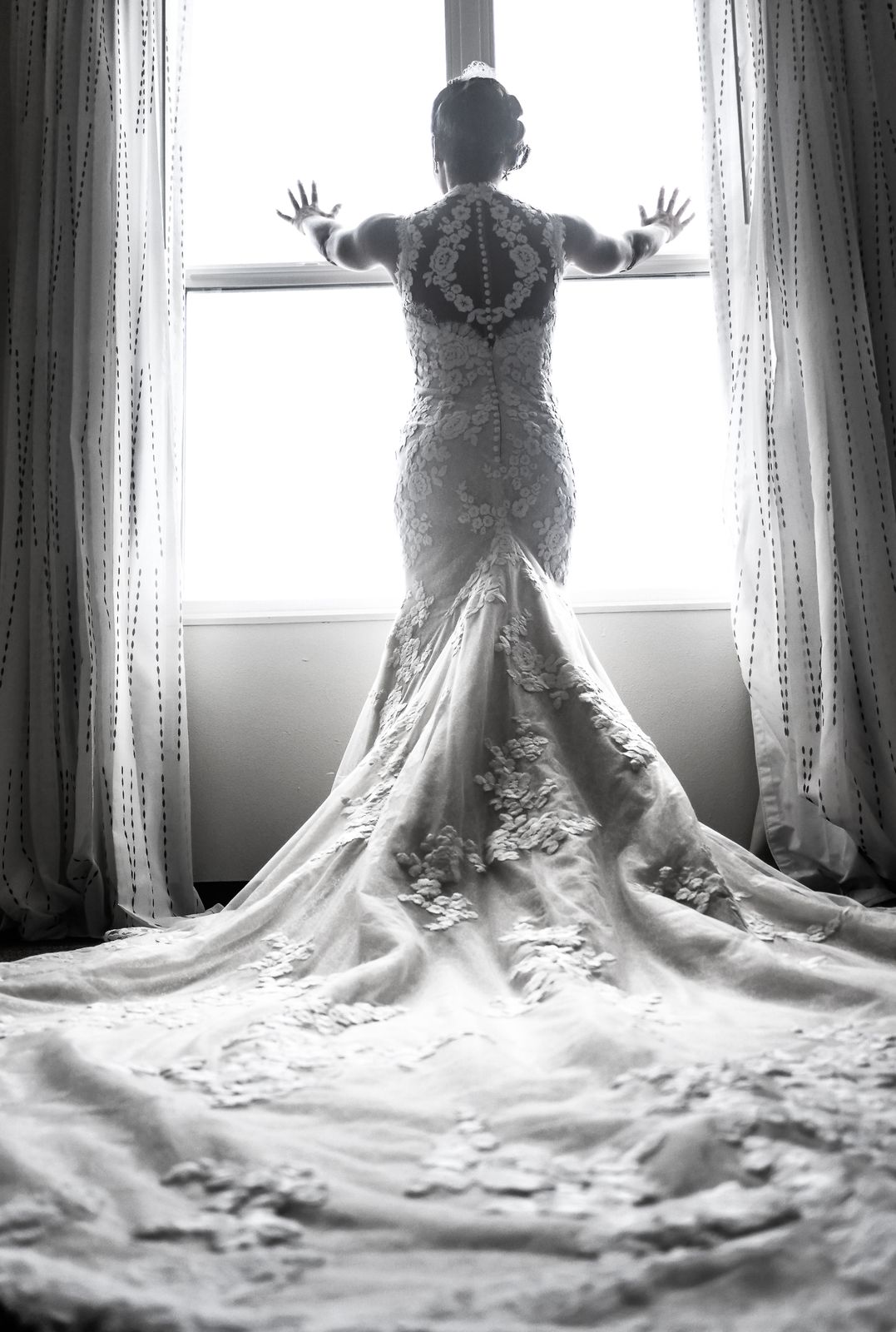 Black-and-white bride at a window, her train fanned on the floor